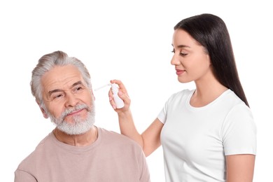 Young woman spraying medication into man's ear on white background