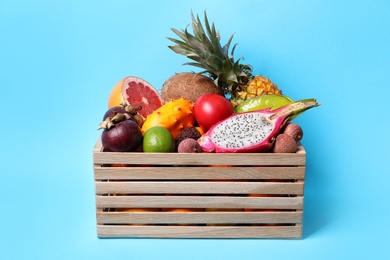 Photo of Different tropical fruits in wooden box on light blue background