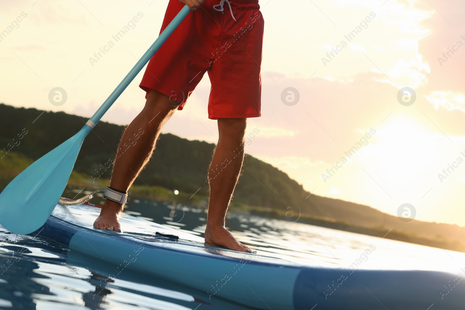 Photo of Man paddle boarding on SUP board in river at sunset, closeup