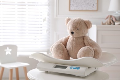 Photo of Baby scales with teddy bear on table in room