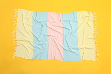 Crumpled striped beach towel on yellow background, top view