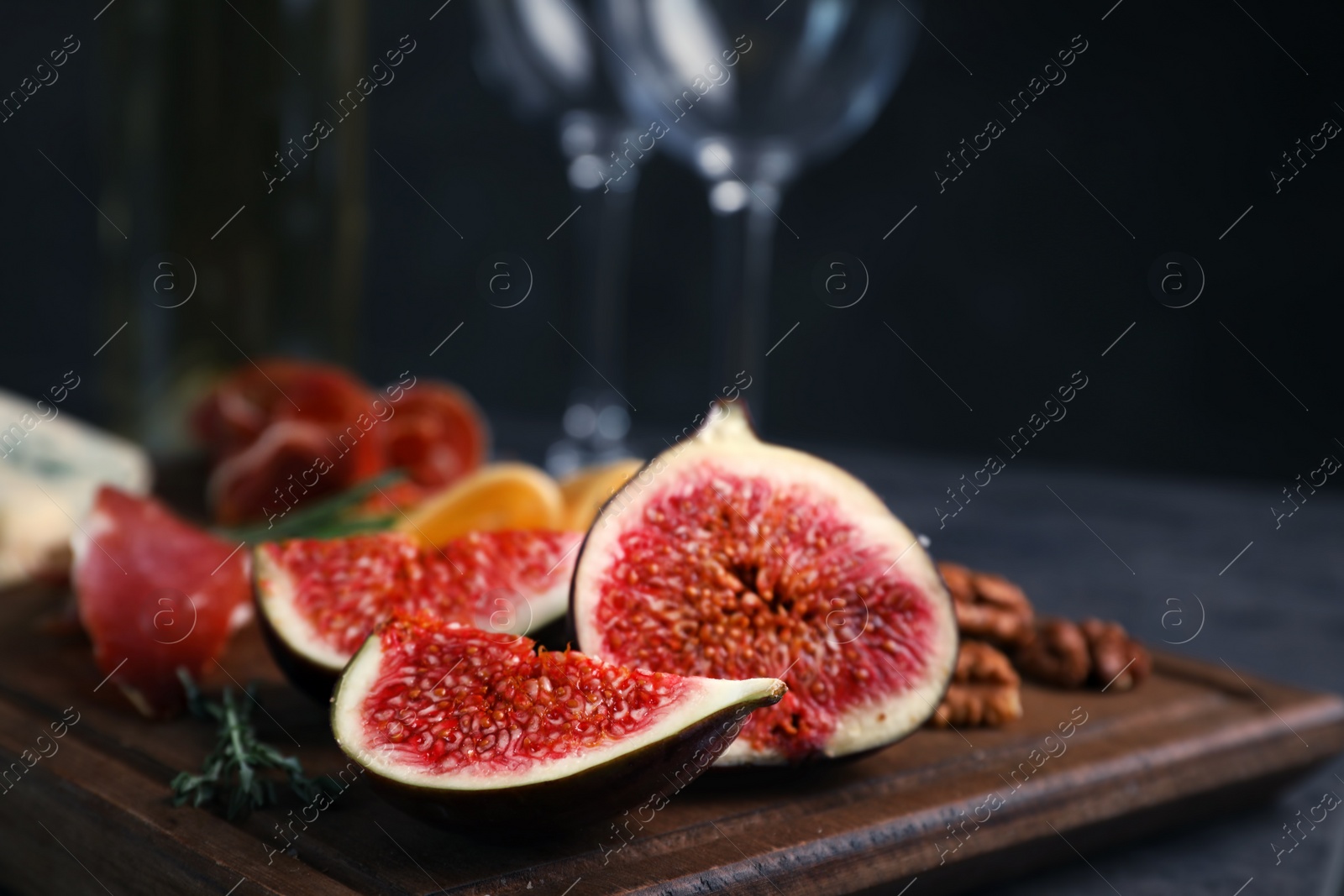 Photo of Wooden board with ripe fig slices on table against dark background, closeup