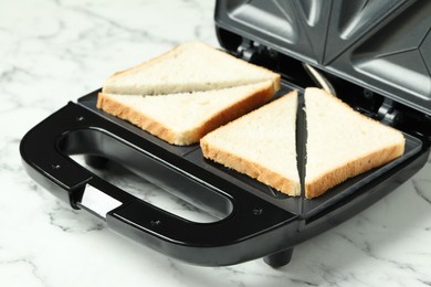 Photo of Modern sandwich maker on white marble table, closeup
