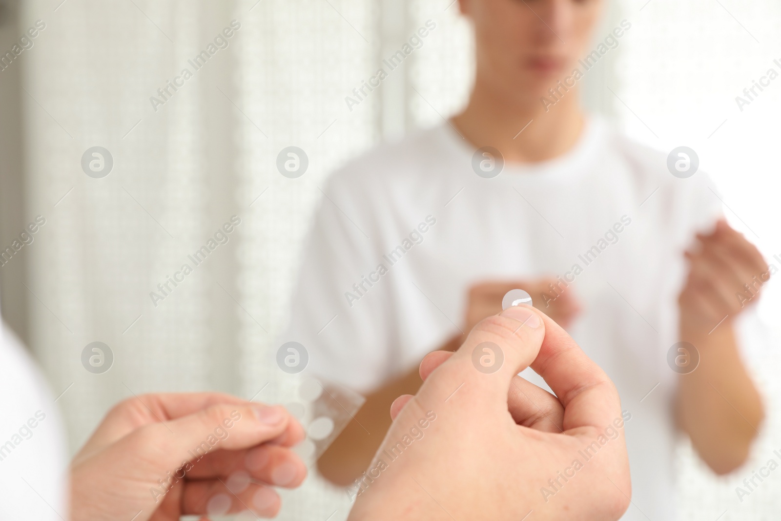 Photo of Teen guy using acne healing patch near mirror indoors, focus on hands
