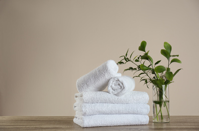 Photo of Clean bath towels and vase with green plants on wooden table. Space for text