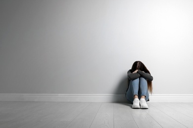 Photo of Upset teenage girl sitting on floor near wall. Space for text