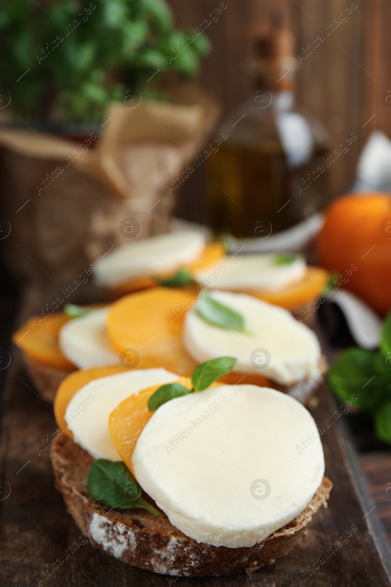 Photo of Delicious sandwiches with mozzarella, yellow tomatoes and basil on wooden board