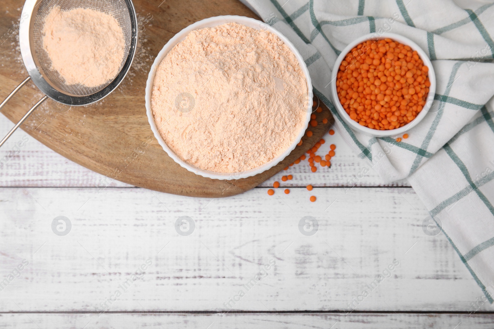 Photo of Bowl of lentil flour and seeds on white wooden table, flat lay. Space for text