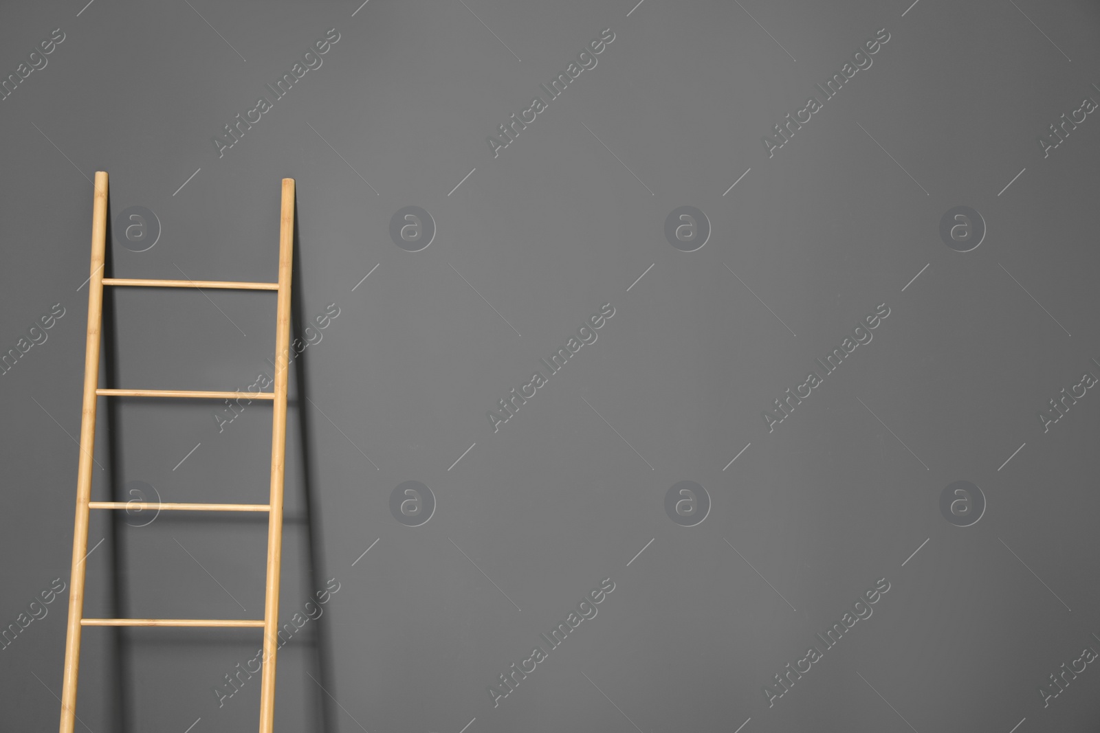 Photo of Modern wooden ladder on grey background. Space for text