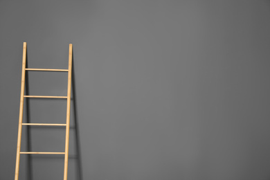 Photo of Modern wooden ladder on grey background. Space for text