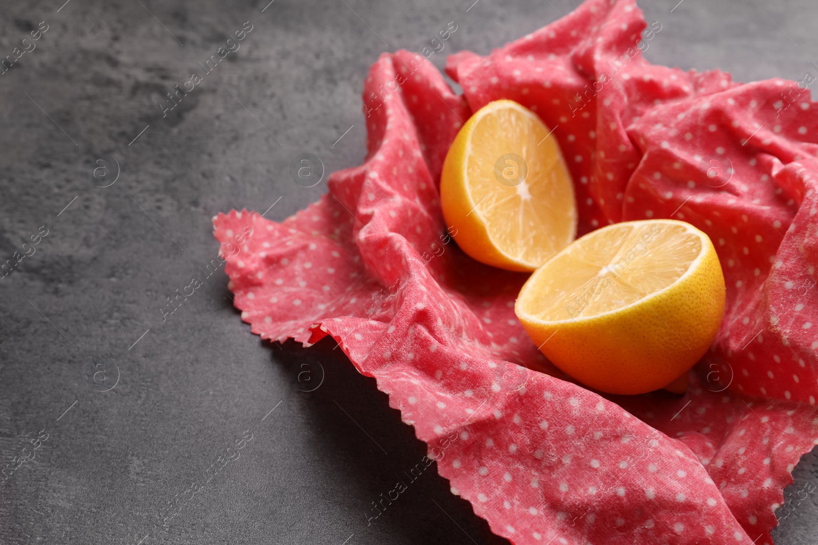 Photo of Halved lemon with beeswax food wrap on grey table, closeup. Space for text