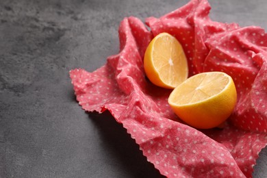 Photo of Halved lemon with beeswax food wrap on grey table, closeup. Space for text