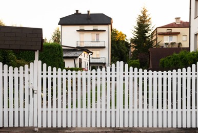 Photo of Houses and trees behind white wooden fence outdoors