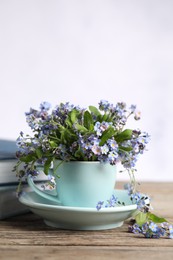 Beautiful forget-me-not flowers in cup and saucer on wooden table against light background