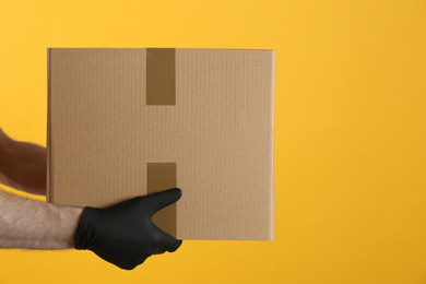 Photo of Courier holding cardboard box on yellow background, closeup. Parcel delivery