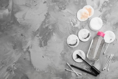 Dirty cotton pads, swabs, mascara and micellar cleansing water on grey background, flat lay. Space for text