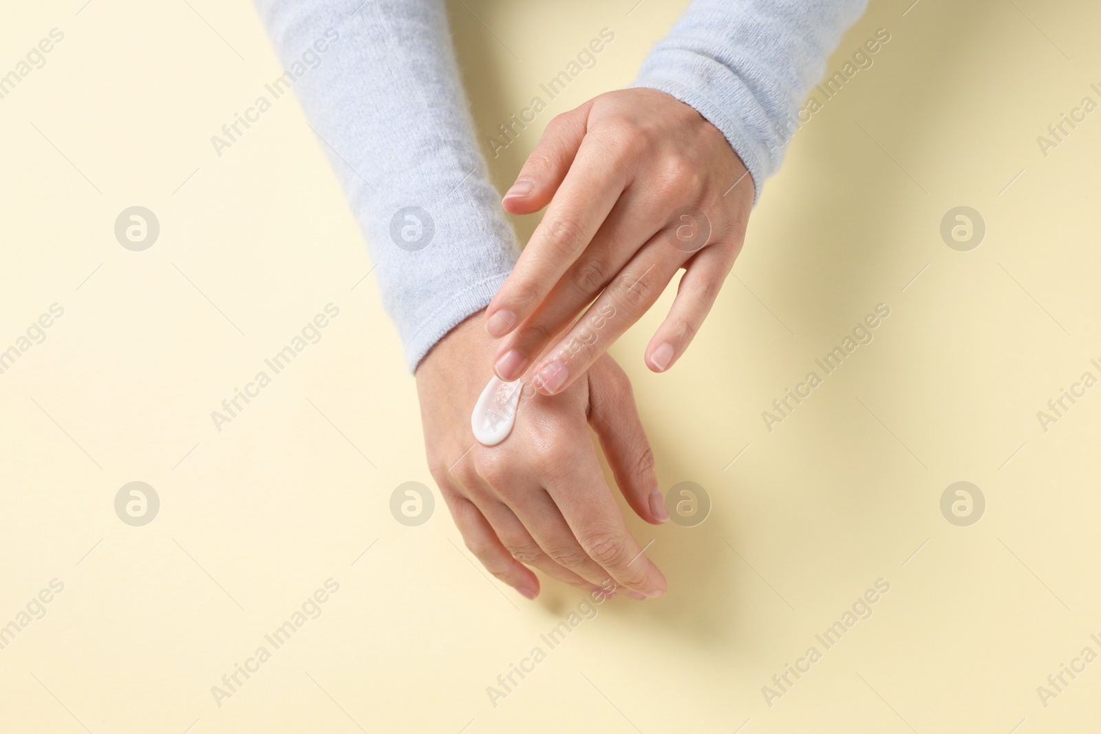 Photo of Woman applying cosmetic cream onto hand on beige background, top view