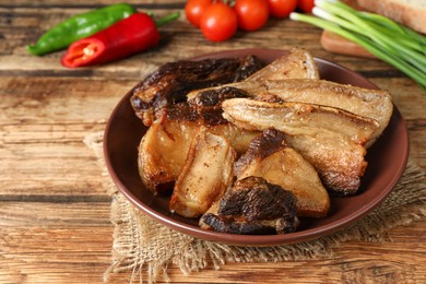 Photo of Tasty fried cracklings on wooden table, closeup. Cooked pork lard