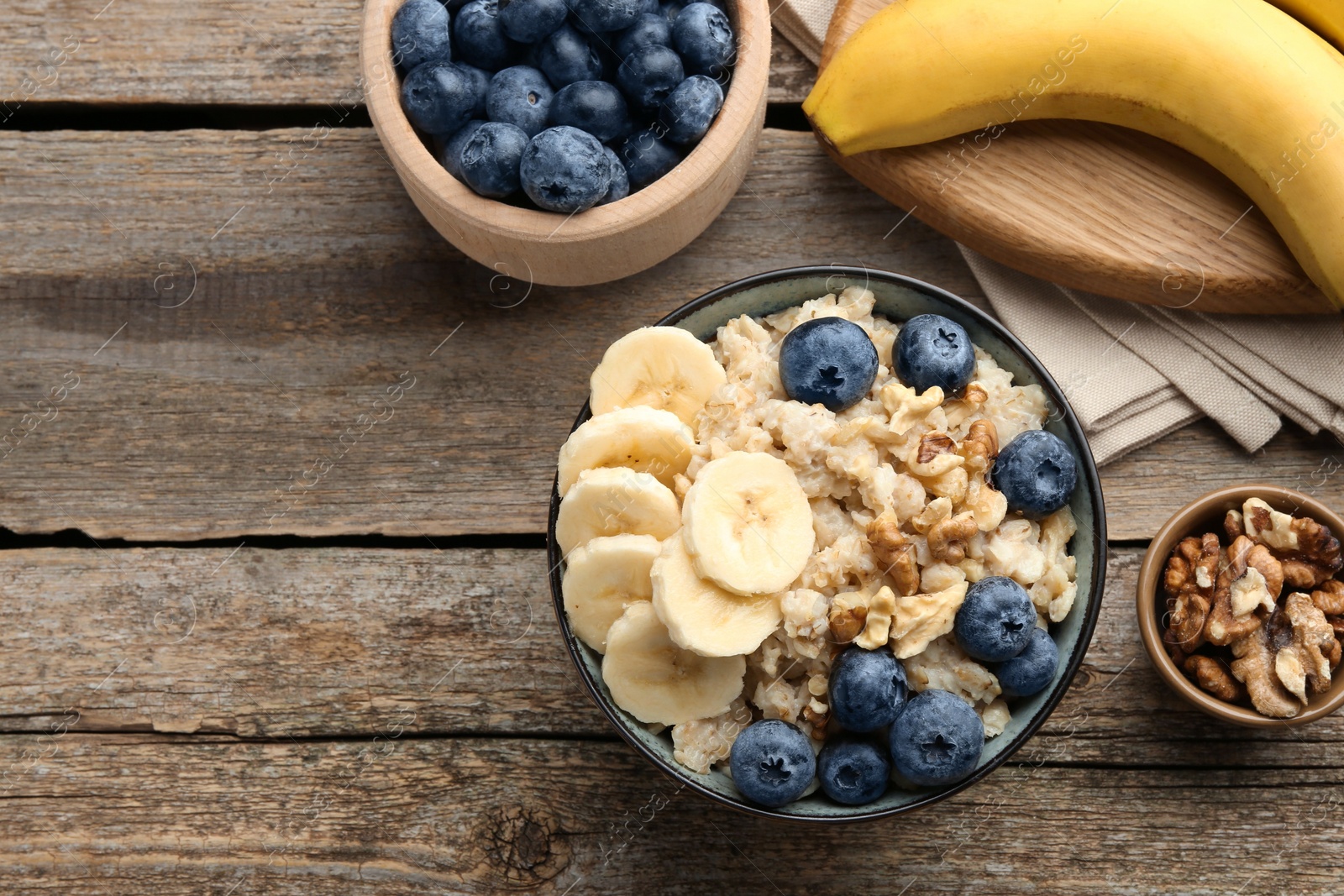 Photo of Tasty oatmeal with banana, blueberries and walnuts served in bowl on wooden table, flat lay. Space for text