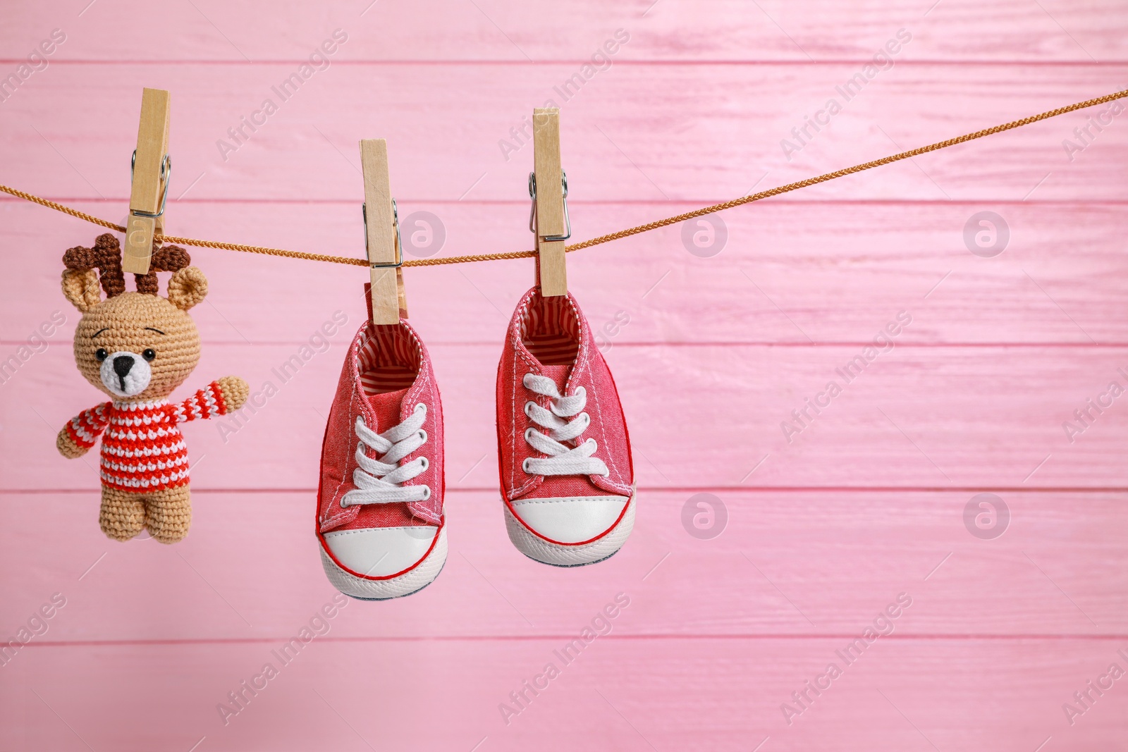 Photo of Cute baby sneakers and crochet toy drying on washing line against pink wooden wall. Space for text