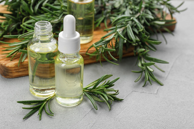 Fresh rosemary and bottles of essential oil on light grey table. Space for text