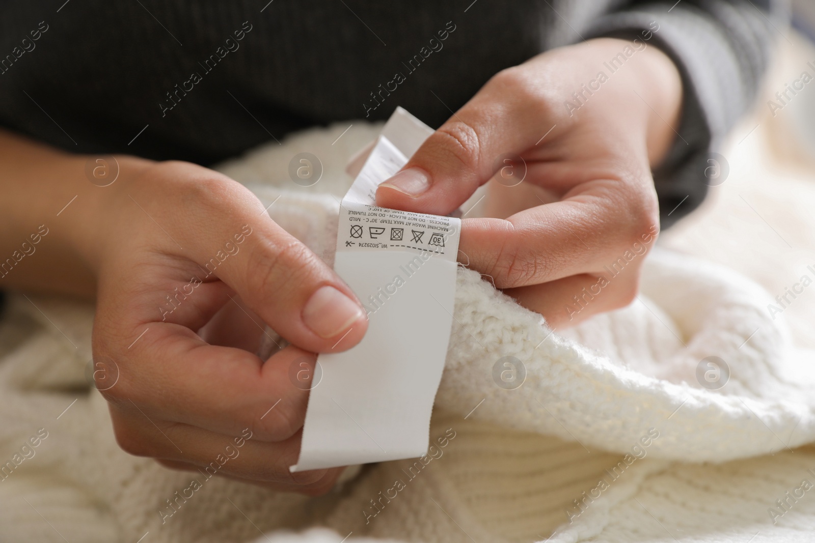 Photo of Woman holding clothing label on white garment, closeup