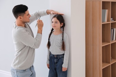 Photo of Father measuring height of his daughter near wall indoors