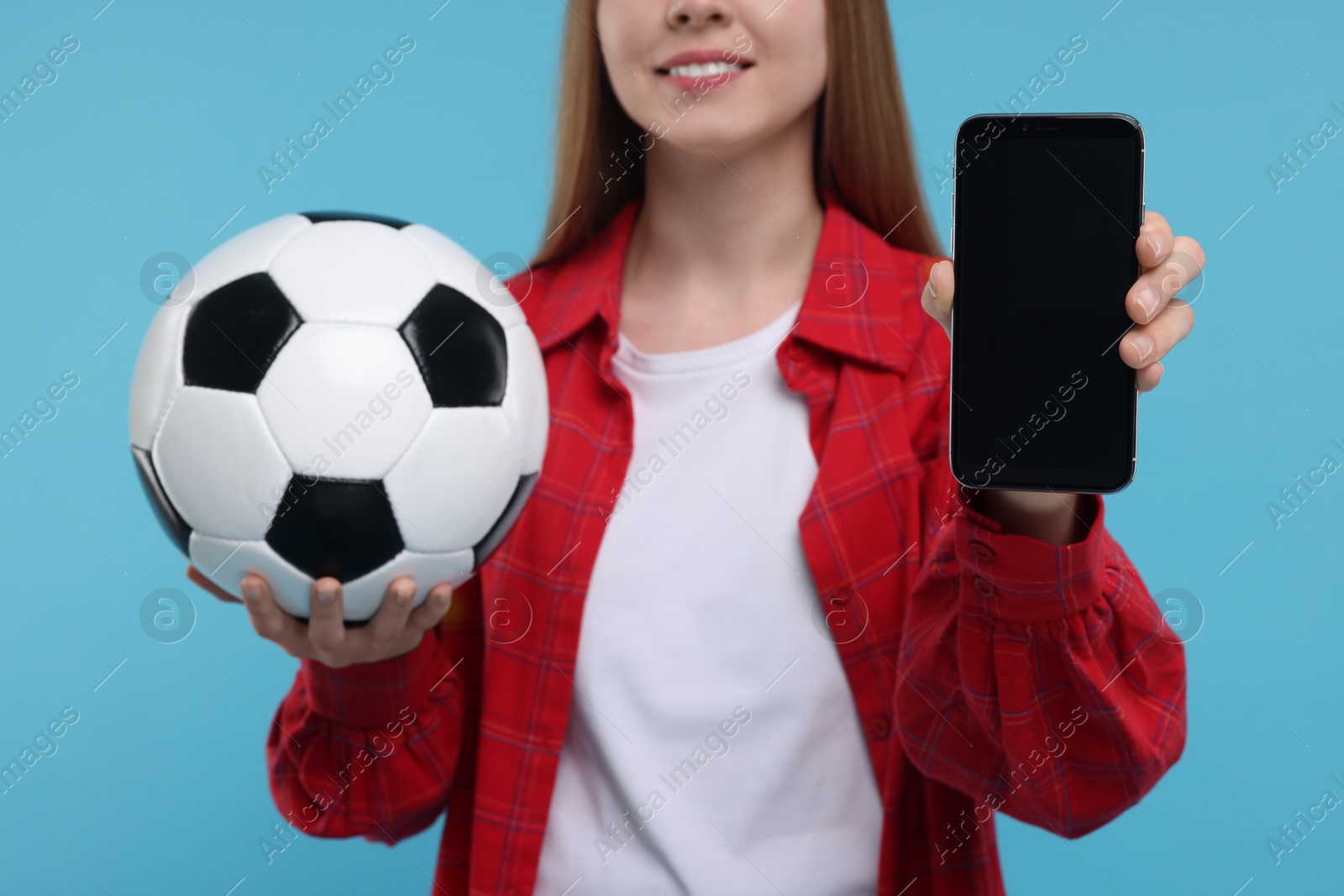 Photo of Sports fan with ball and smartphone on light blue background, closeup