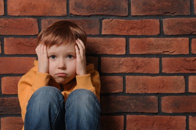 Photo of Upset boy sitting near brick wall, space for text. Children's bullying
