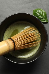 Photo of Cup of fresh green matcha tea with bamboo whisk on black table, top view