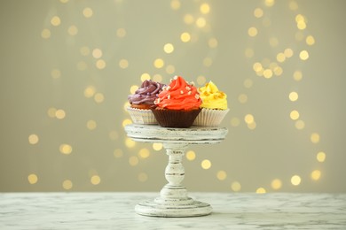 Photo of Different colorful cupcakes on white marble table against blurred lights