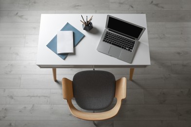 Photo of Laptop and office stationery on white table near armchair in room, above view