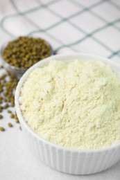 Photo of Mung bean flour in bowl and seeds on white table, closeup