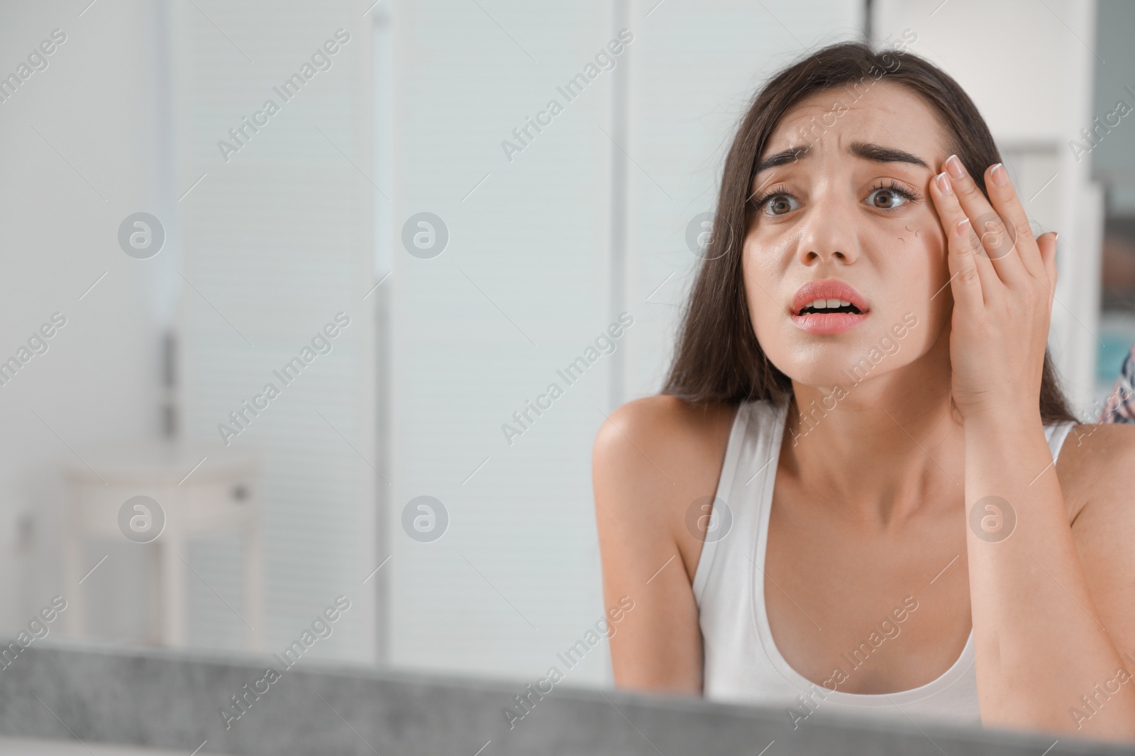 Photo of Young woman with eyelash loss problem looking in mirror indoors