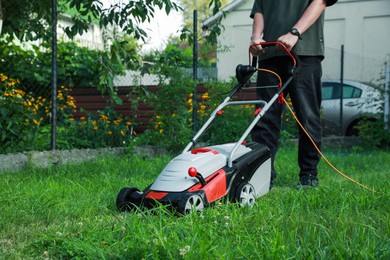 Photo of Man cutting grass with lawn mower in garden, closeup