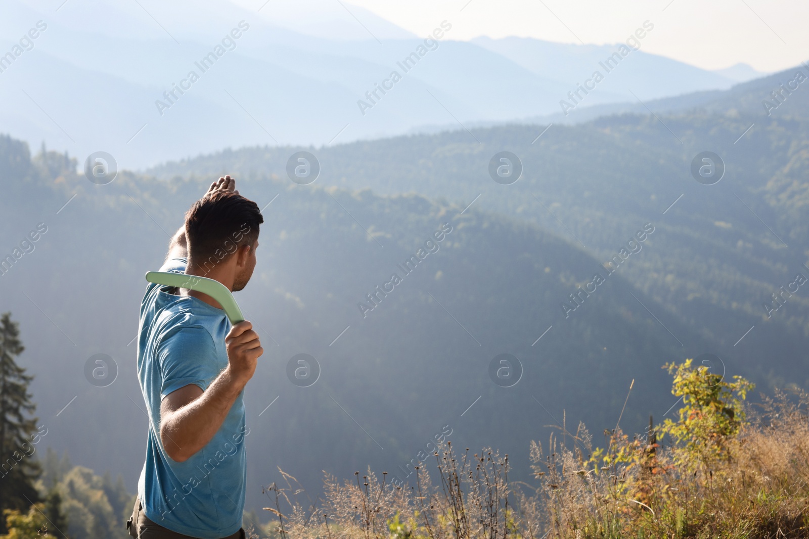 Photo of Man throwing boomerang in mountains on sunny day, space for text