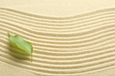 Photo of Zen rock garden. Wave pattern and green leaf on beige sand, top view