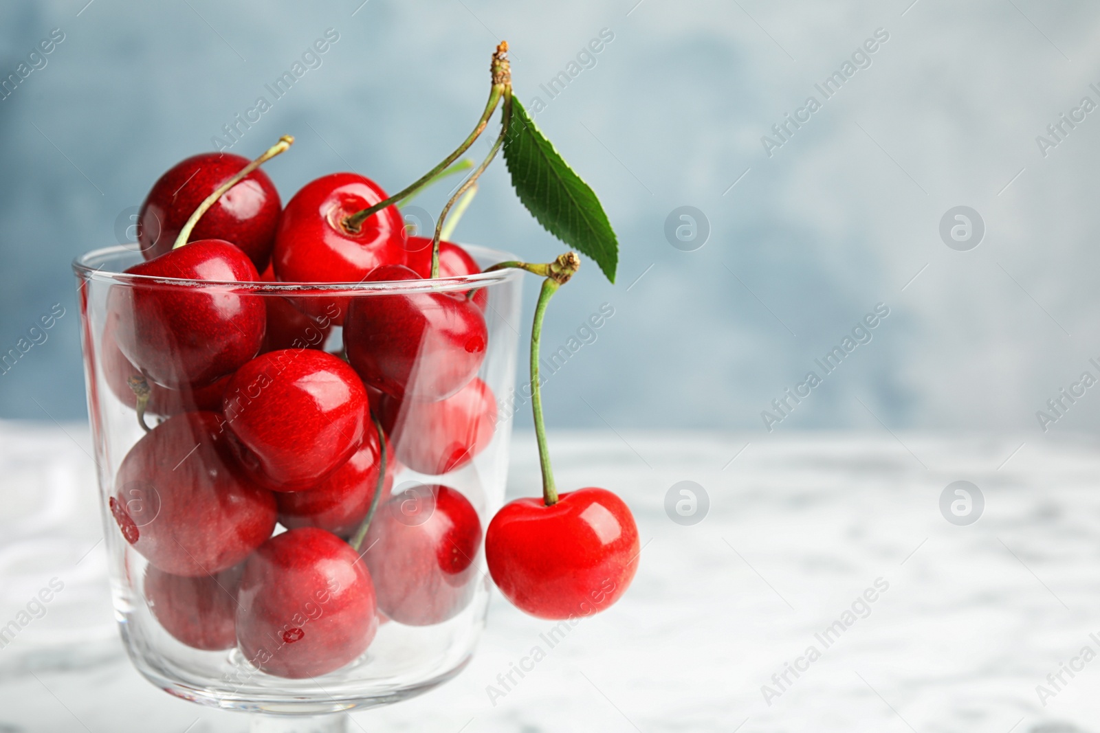 Photo of Glass dessert bowl with ripe sweet cherries on marble table