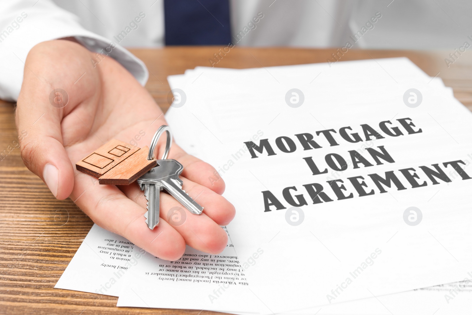 Image of Mortgage loan agreement. Man holding house keys in hand over table, closeup