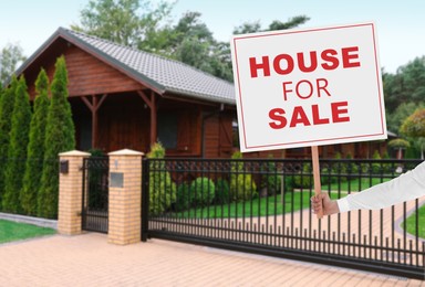 House for sale. Woman holding signboard near beautiful house outdoors, closeup