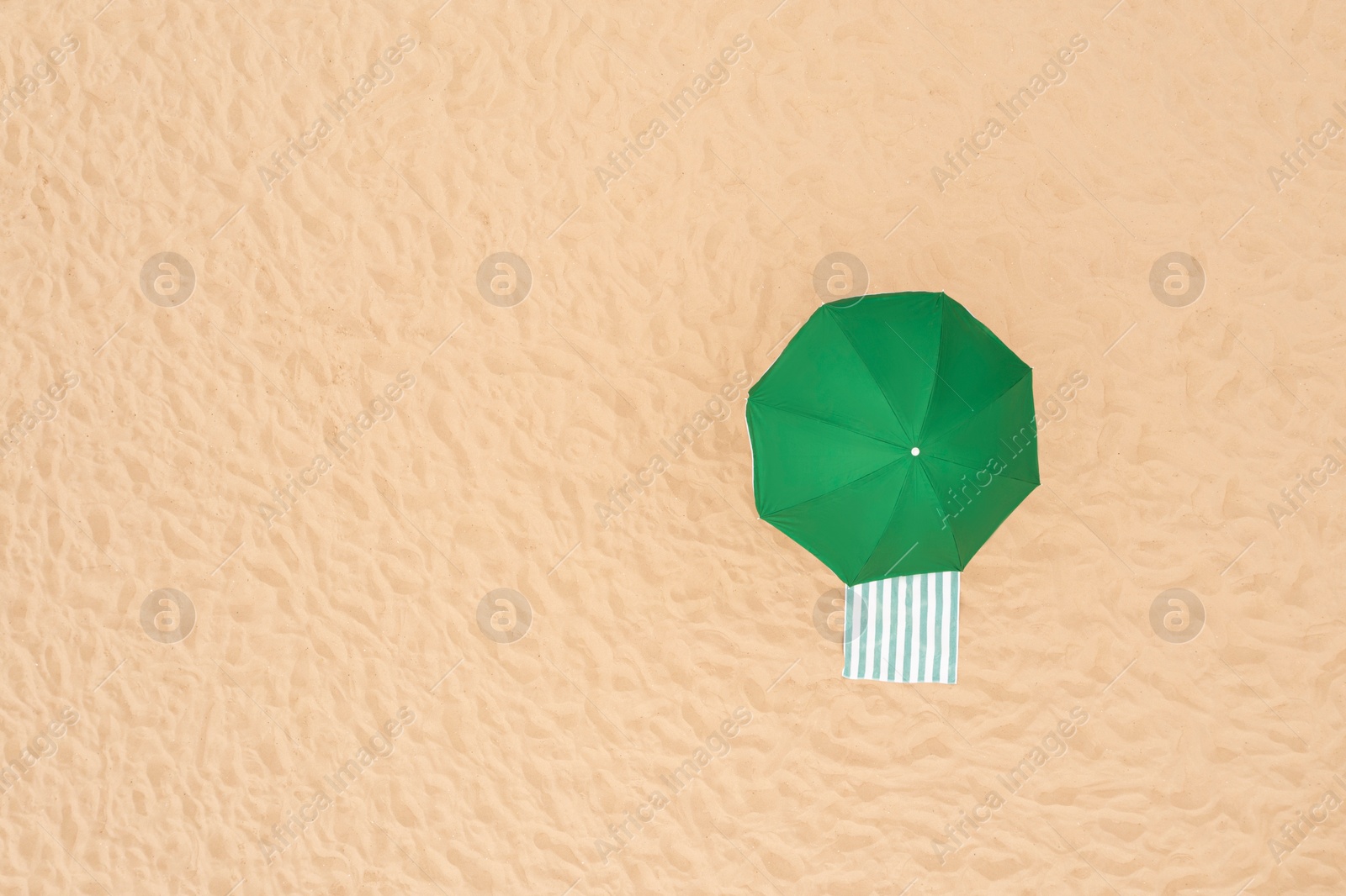 Image of Green beach umbrella and towel on sandy coast, aerial view. Space for text