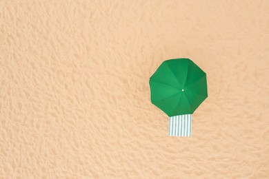 Green beach umbrella and towel on sandy coast, aerial view. Space for text