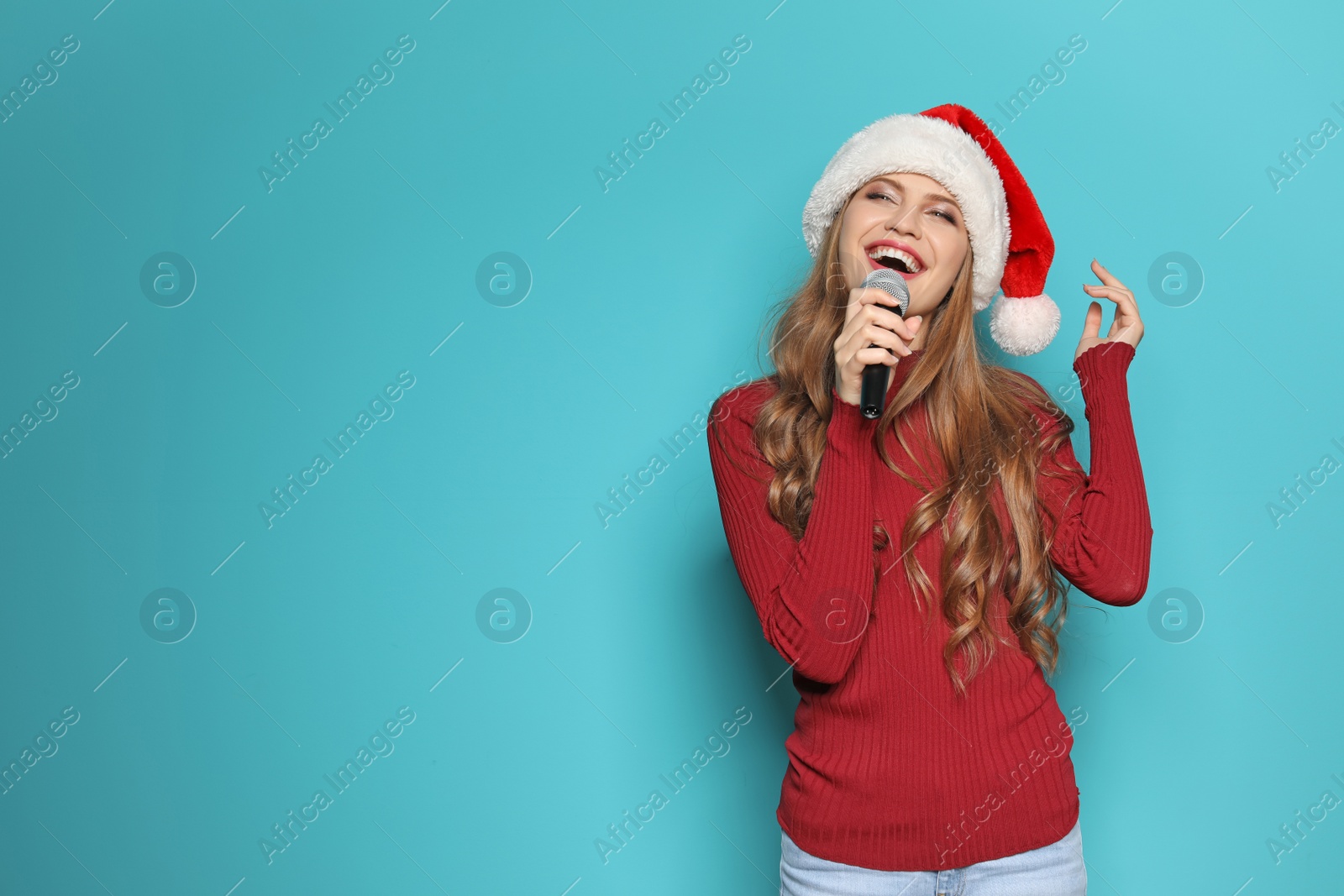 Photo of Young woman in Santa hat singing into microphone on color background. Christmas music