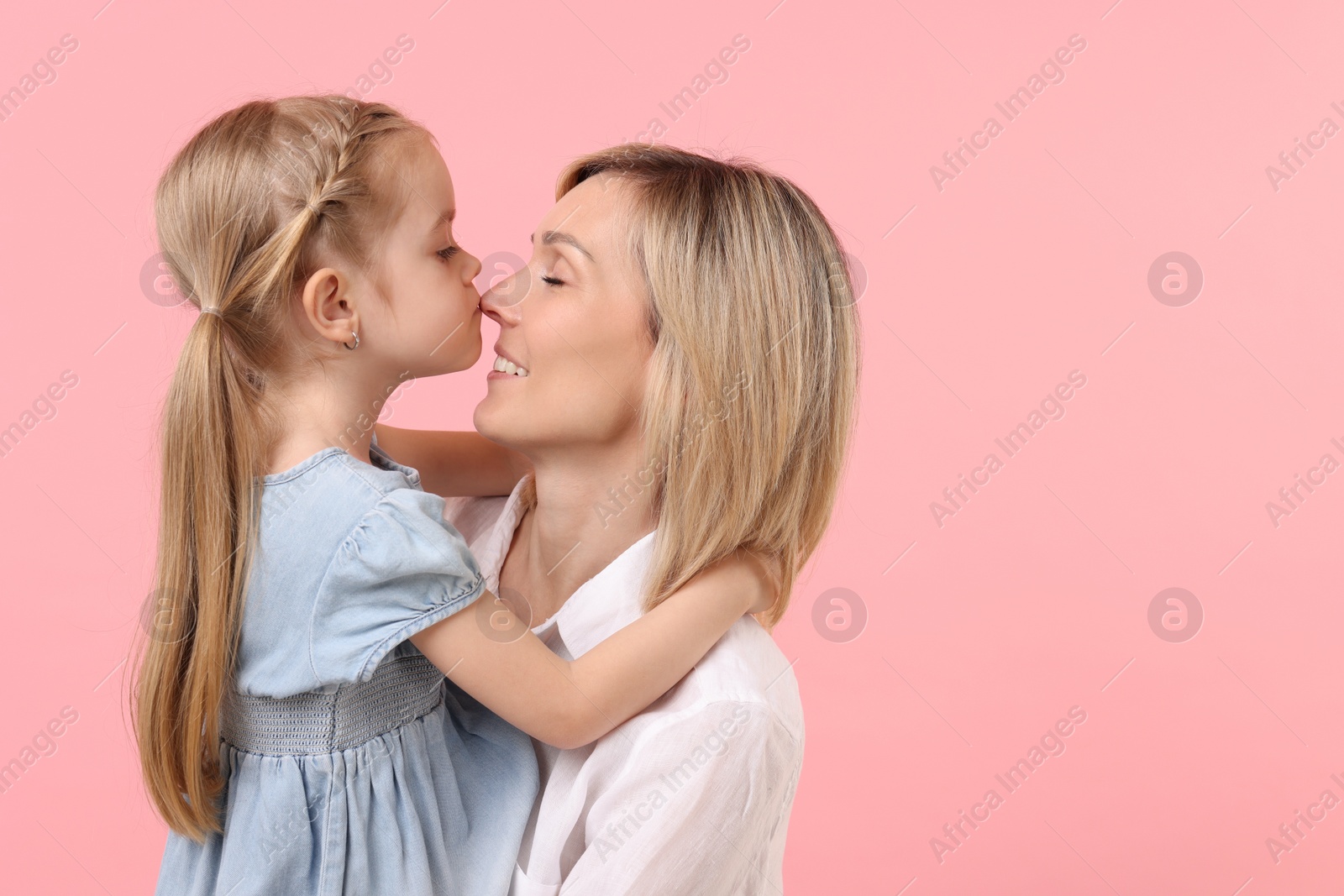 Photo of Daughter hugging and kissing her happy mother on pink background. Space for text