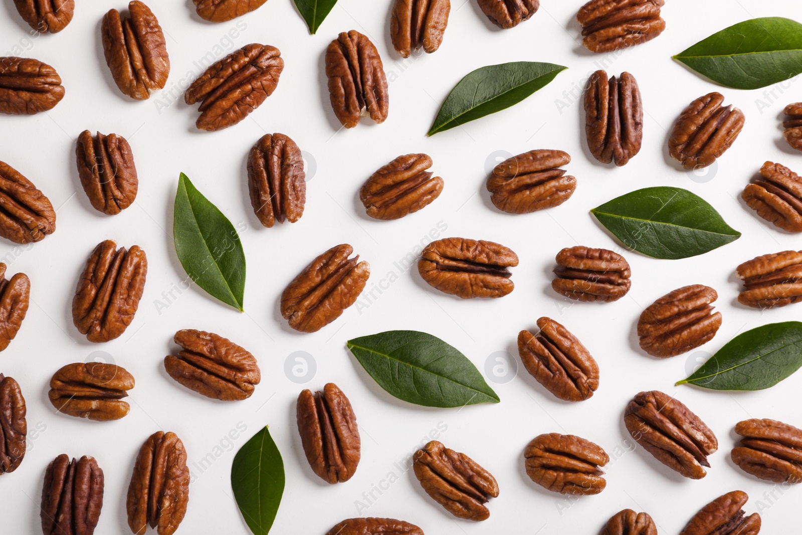 Photo of Delicious pecan nuts and green leaves on white background, flat lay