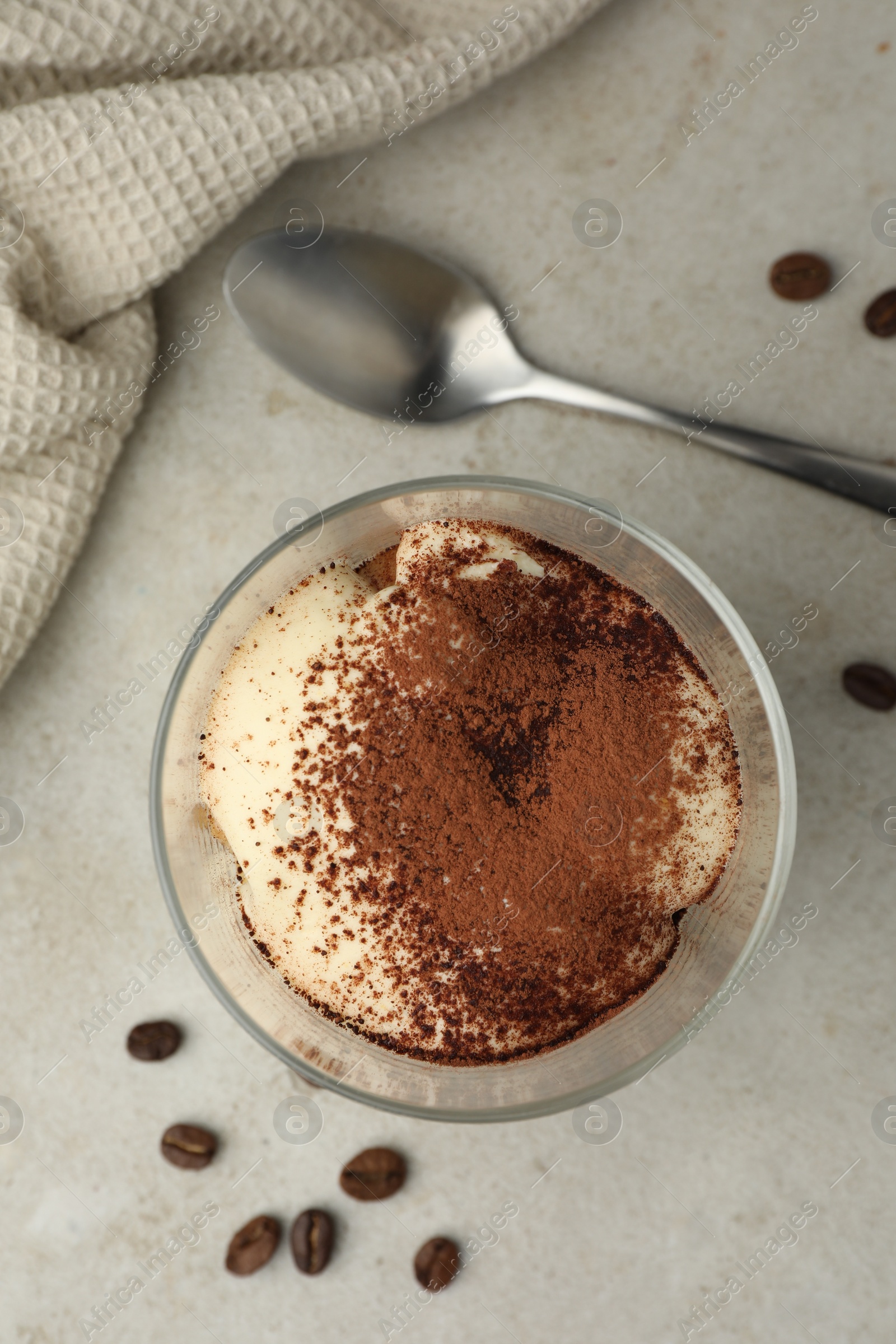 Photo of Delicious tiramisu in glass, spoon and scattered coffee beans on light table, flat lay