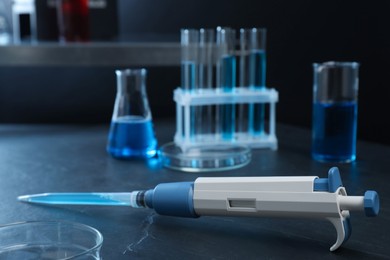 Laboratory analysis. Micropipette with liquid and different glassware on black table