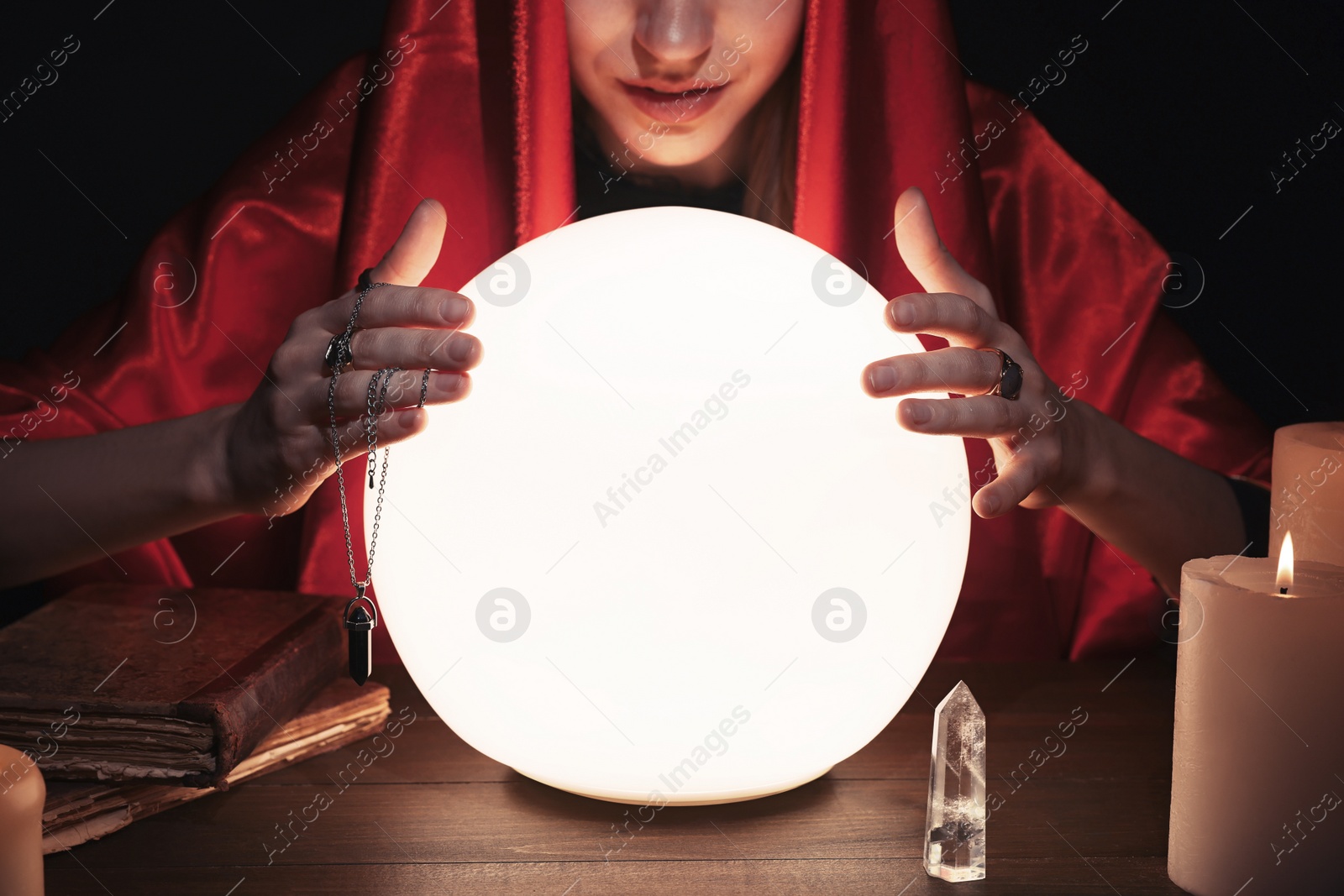 Photo of Soothsayer using glowing crystal ball to predict future  at table in darkness, closeup. Fortune telling