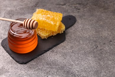 Photo of Sweet golden honey in jar, dipper and pieces of honeycomb on grey textured table, space for text