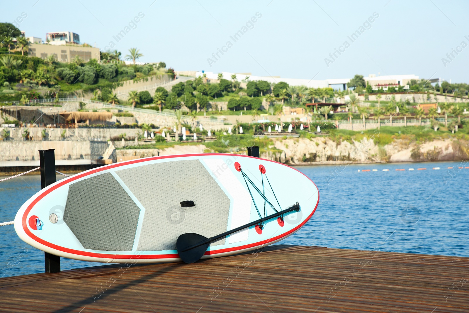 Photo of SUP board with paddle on wooden pier near sea